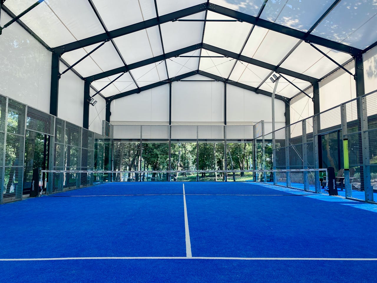 Spacious indoor pádel court with vibrant blue flooring under a wide roof.