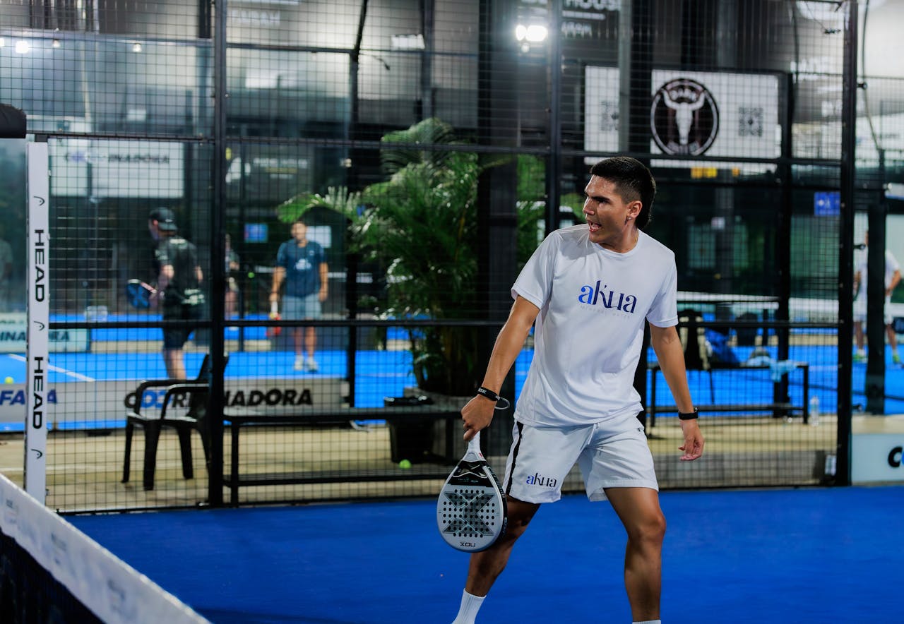 Energetic pádel tennis player at indoor court mid-match.